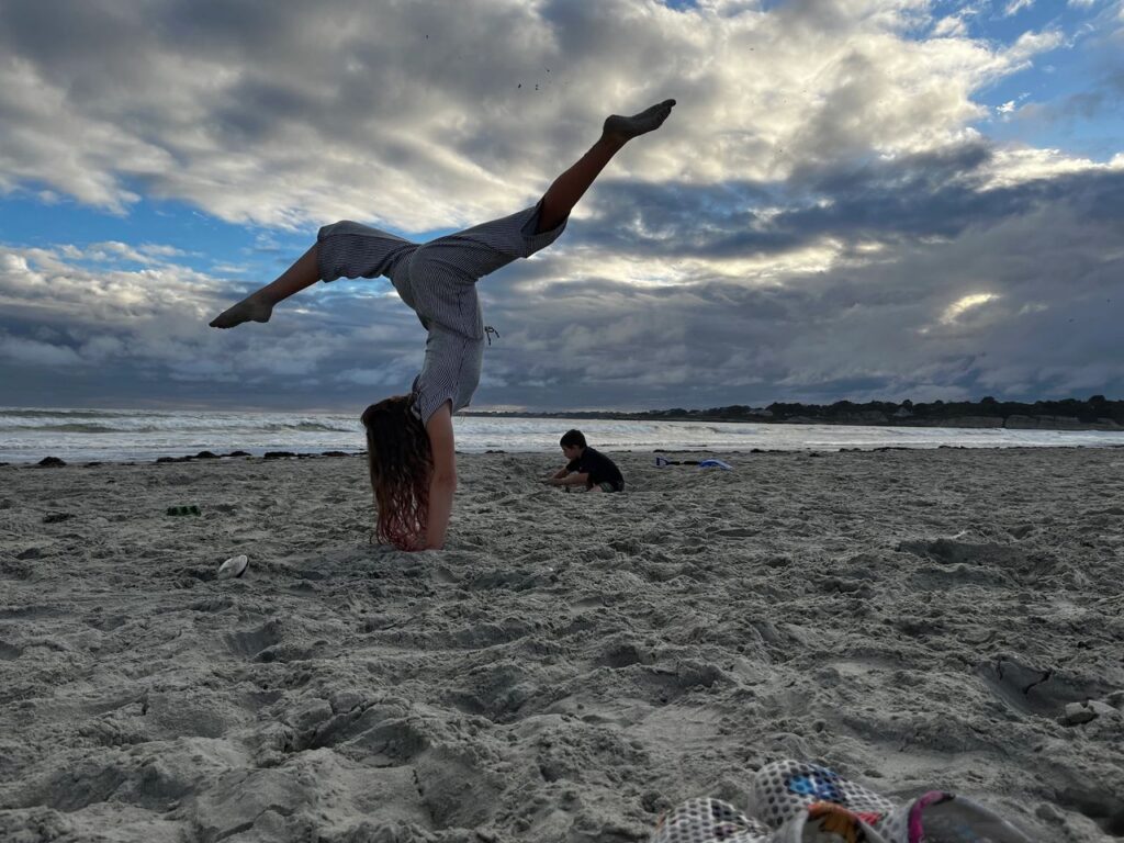 Person doing a handstand on cloudy beach sand.