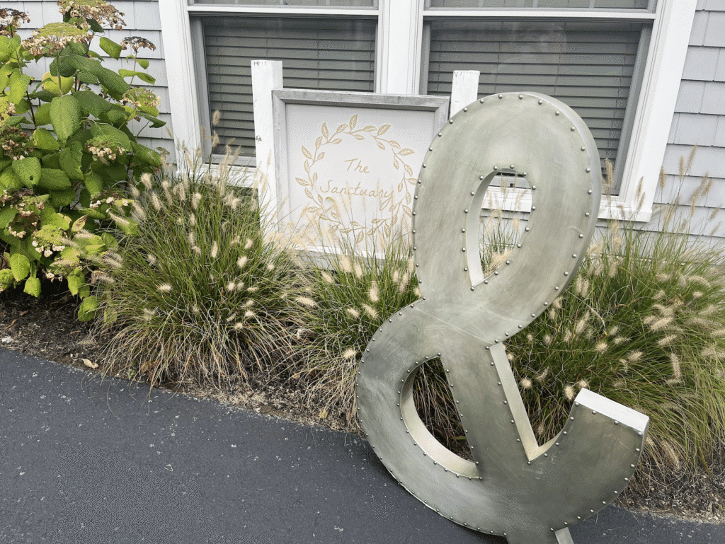 Large metal ampersand decoration outdoors near plants and windows.