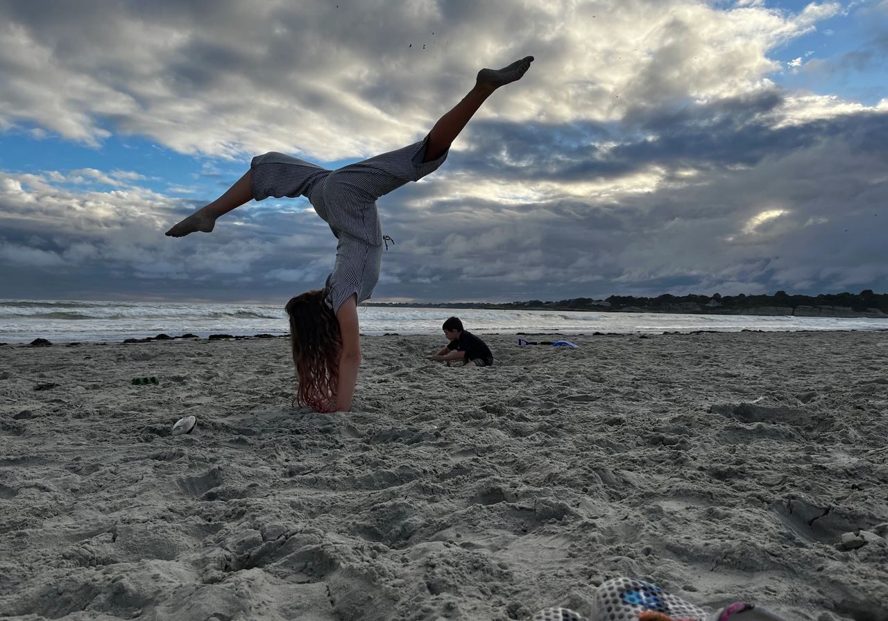 Person doing a handstand on cloudy beach sand.
