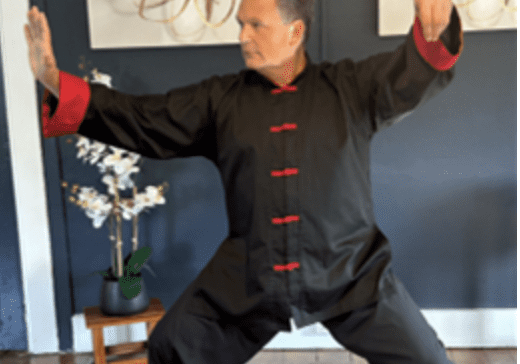 A man practicing Tai Chi in traditional attire indoors.