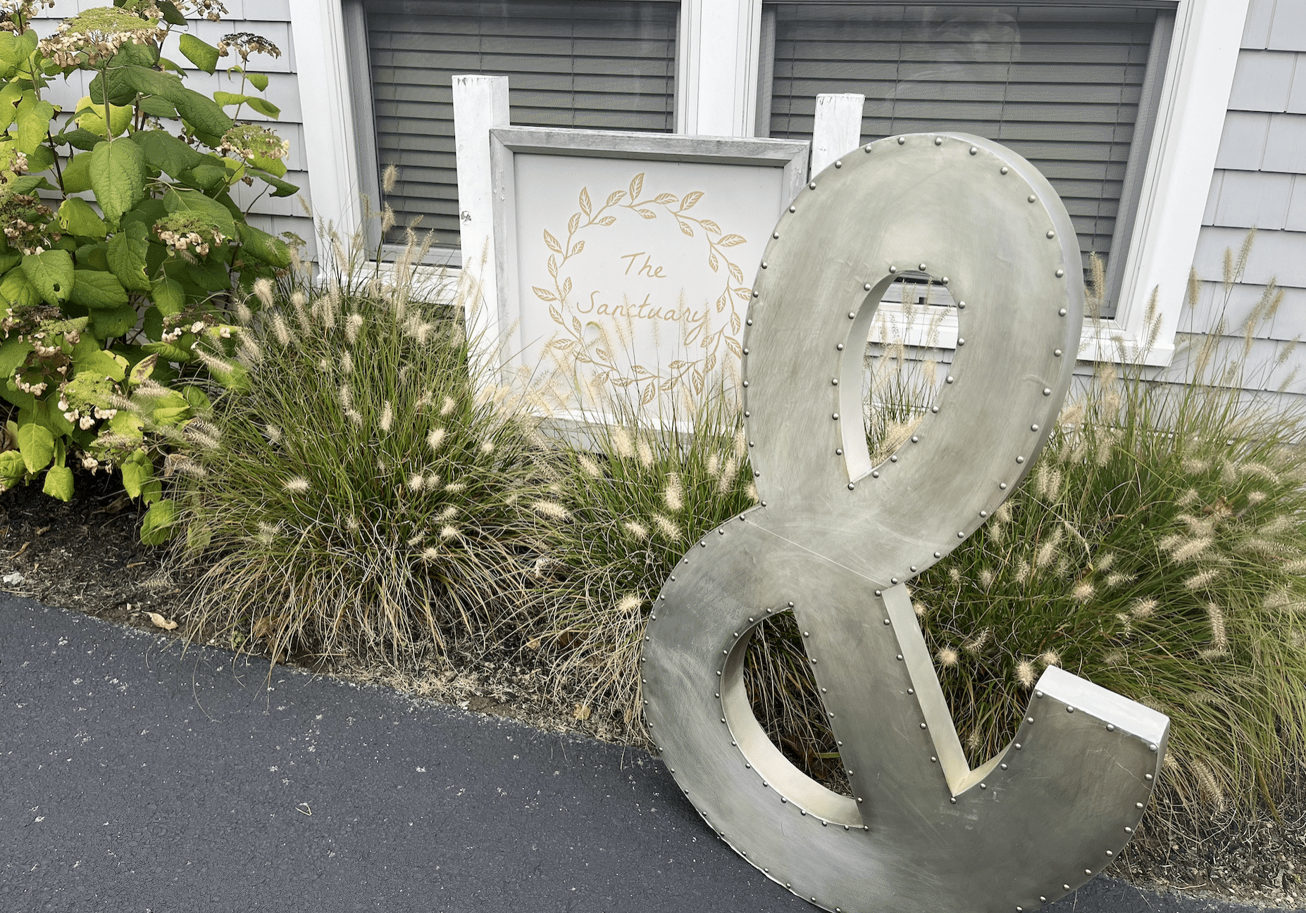 Large metal ampersand decoration outdoors near plants and windows.